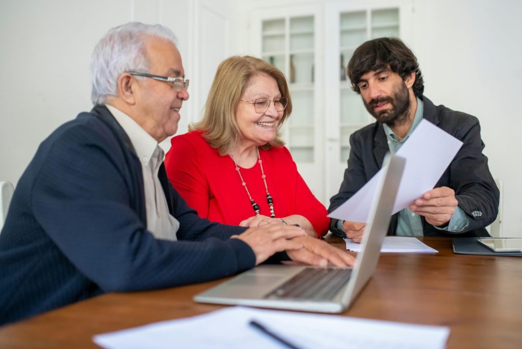 Diverse group discussing documents around a laptop indoors, showcasing teamwork and collaboration.